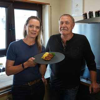 Rainer Limmer und Susanne Nett und die gekochten Frikadellen mit Kartoffelsalat auf einem Teller.