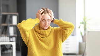 Frau hält mit schmerverzerrtem Gesicht ihren Kopf