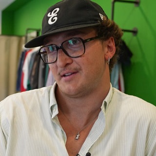 Jason Bonk sitzt in seinem Second-Hand-Laden in Koblenz vor Kleiderstangen.