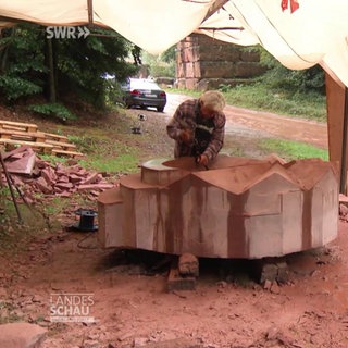 Ein Bildhauer meiselt an einem großen Stein unter einer Zeltplane