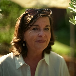 Frau steht neben einem Olivenbaum