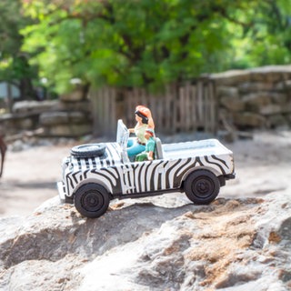 "Little People"- Figuren in einem Safariauto vor einem Kamel.
