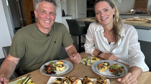 Alexander Heinrich und Susanne Nett sitzen am Tisch, mit Kartoffel-Spinatschnecken auf dem Teller.