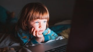 Kind sitzt vor hell erleuchtetem Computermonitor