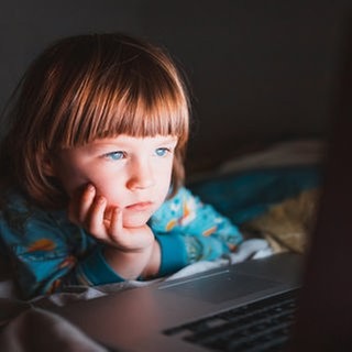 Kind sitzt vor hell erleuchtetem Computermonitor
