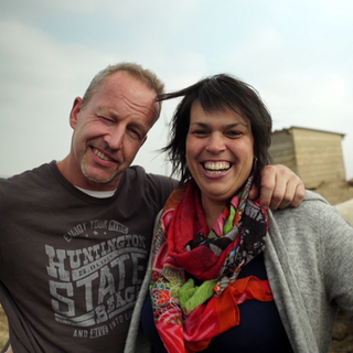 Mann und Frau stehen auf einem Fled mit Schweinen im Hintergrund.