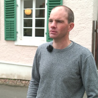 Mann steht vor seinem denkmalgeschützen Wohnhaus in der Eifel.