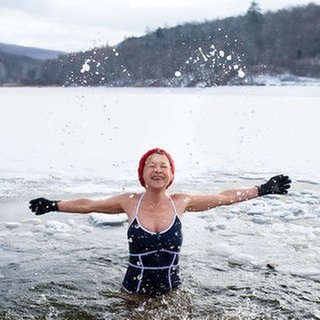 Frau steht im Badeanzug, mit Handschuhen und Mütze im Wasser