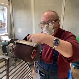 Ein Mann schleift einen Kirner Edelstahlgrill-Rost