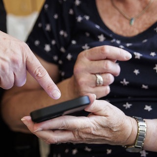 Ein Finger deutet auf das Handy einer älteren Frau