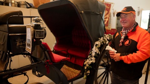 Mann steht neben einer restaurierten Kutsche