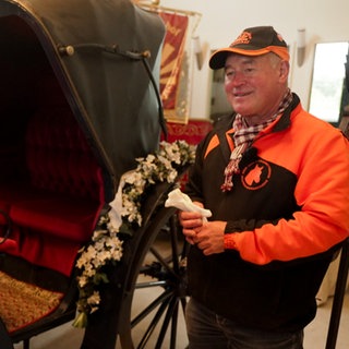 Mann steht neben einer restaurierten Kutsche