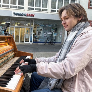 Straßenpianist sitzt in der Trierer Fußgängerzone am Klavier.