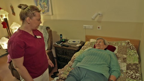Helga Dörhöfer erhält Hilfe von einer Pflegekraft in ihrem Zimmer im Pflegeheim