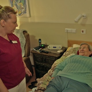 Helga Dörhöfer erhält Hilfe von einer Pflegekraft in ihrem Zimmer im Pflegeheim