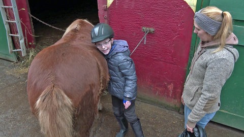 Der kleine Ben lehnt sich an einen Pferderücken