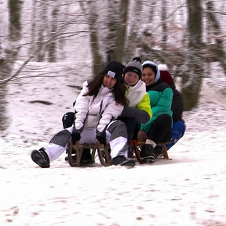 Drei Mädchen auf einem Schlitten fahren bergab.