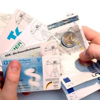 Zwei Hände halten Versichertenkarten und Geld