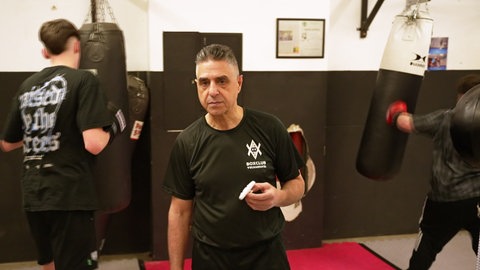 Mann steht in einem Boxklub mit trainiertenden Kindern im Hintergrund