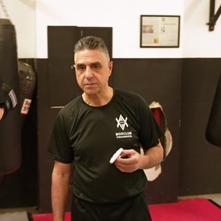 Mann steht in einem Boxklub mit trainiertenden Kindern im Hintergrund