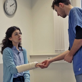 Ein Mann im Arztkittel betrachtet den Gipsarm einer Frau