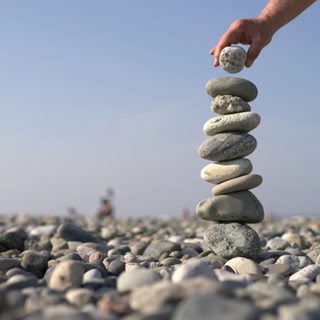 Eine Hand setzt ein Steinchen auf ein Steintürmchen oben drauf