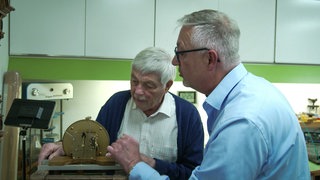 Zwei Männer arbeiten an einem Uhrwerk