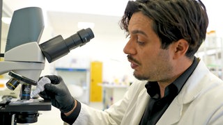 Gründer Dr. Bayram Cucu trägt einen Laborkittel und arbeitet am Mikroskop.