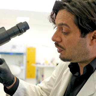 Gründer Dr. Bayram Cucu trägt einen Laborkittel und arbeitet am Mikroskop.
