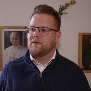 Mann steht vor zwei gerahmten Bildern von Päpsten