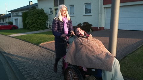 Frau schiebt Kind im Rollstuhl auf der Straße