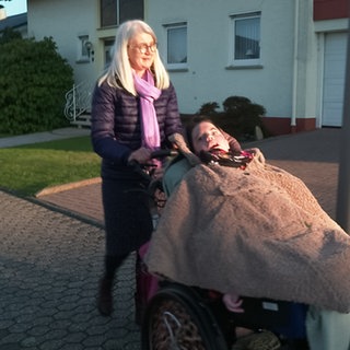 Frau schiebt Kind im Rollstuhl auf der Straße