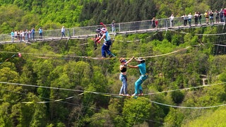 Slackliner balancieren neben der Geierlay-Brücke.