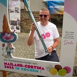 Mann steht mit einer olympischen Fackel in Cochemer Innenstadt.