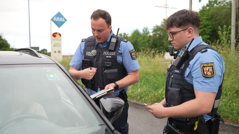 Zwei Polizeibeamte befragen eine Autofahrer auf einer Raststätte