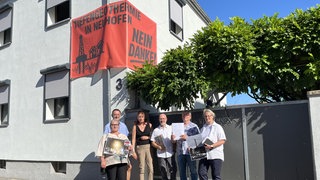 Menschen stehen vor einem roten Plakat, darauf steht: Tiefengeothermie in Neuhofen - Nein Danke!