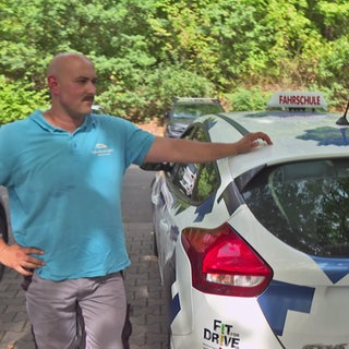 Fahrschüler mit Fahrlehrer am Fahrschulauto