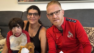Mutter, Vater und Kind mit Behinderung sitzen auf einem Sofa