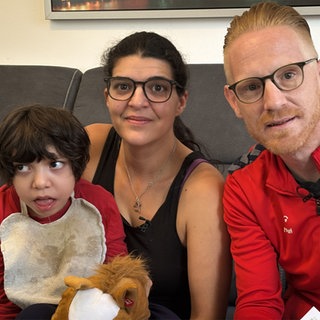 Mutter, Vater und Kind mit Behinderung sitzen auf einem Sofa