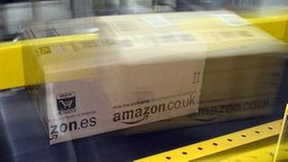 Ein Amazon-Paket fährt auf einem Fließband. Es ist in kurzem Abstand zweimal fotografiert worden, sodass es verschwommen aussieht.