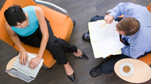 Mann und Frau arbeiten im Büro mit Laptop und Papier.