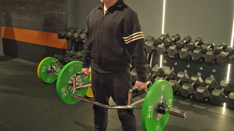Ein Mann macht Kraftsport. Beim Kreuzheben ist es wichtig, schulterbreit zu stehen. Von dort aus geht man mit Gewichten in die Hocke, der Rücken sollte dabei gerade bleiben. Im Stand sollte der Po angespannt werden. 