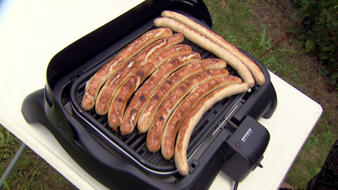 Ein Elektrogrill mit noch rohen Würstchen auf dem Rost.