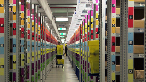 Regale eines Amazon-Lagers, dazwischen ein Mitarbeiter.