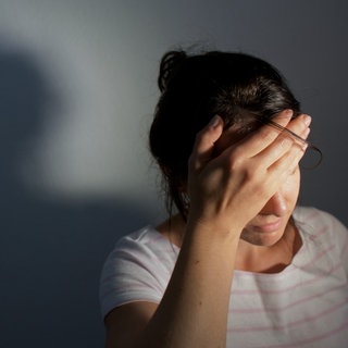 Junge Frau fasst sich an die Stirn. Manchmal sind Menschen nach einer schweren Corona-Erkrankung von Long Covid betroffen.