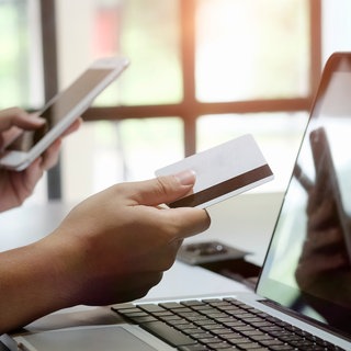 Symbolbild: Eine Person sitzt mit Smartphone und EC-Karte vor einem Laptop