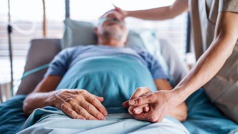 Ein Patient liegt im Krankenbett und wird von einem Arzt behandelt. 