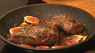 Rehsteak bruzelt in Rotwein-Soße zuasmmen mit geviertelten Feigen in einer Pfanne.