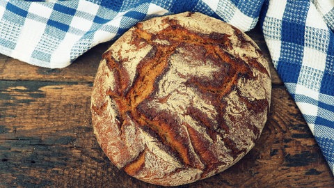 Brotlaib liegt auf einem Holzbrett. Dinkel ist nicht per se gesünder als Weizen.