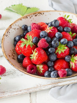 In einer weißen Schale liegen verschiedene Beerensorten: Heidelbeeren, Erdbeeren und Himbeeren